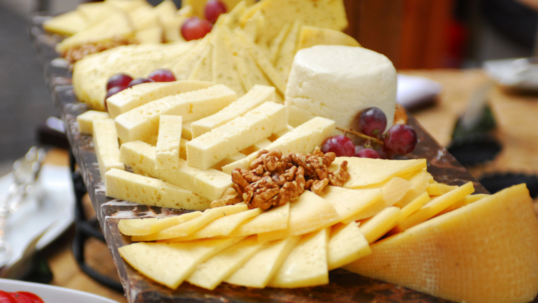 Close-up of a winter cheese board with sliced aged cheeses, soft white cheese, walnuts, and red grapes arranged on a rustic serving board.