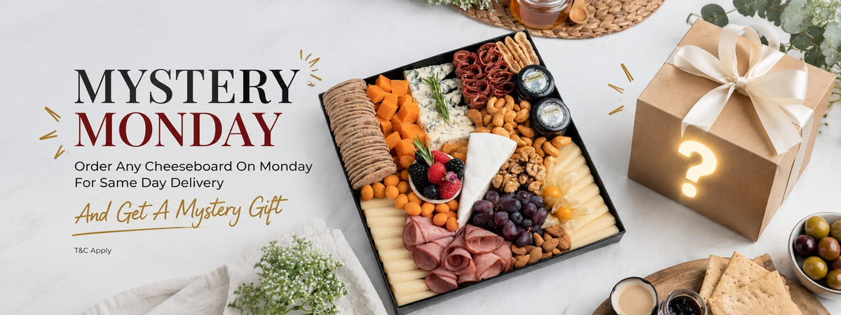 Mystery Monday is a promotional campaign visual showing a generously arranged cheese board with assorted cheeses, cured meats, crackers, fruits, nuts, and gourmet accompaniments, paired with a wrapped mystery gift. Discover cheeseboard Dubai, cheese platter Dubai, and charcuterie Dubai from The Cheese Man. Enjoy fresh delivery across the UAE.