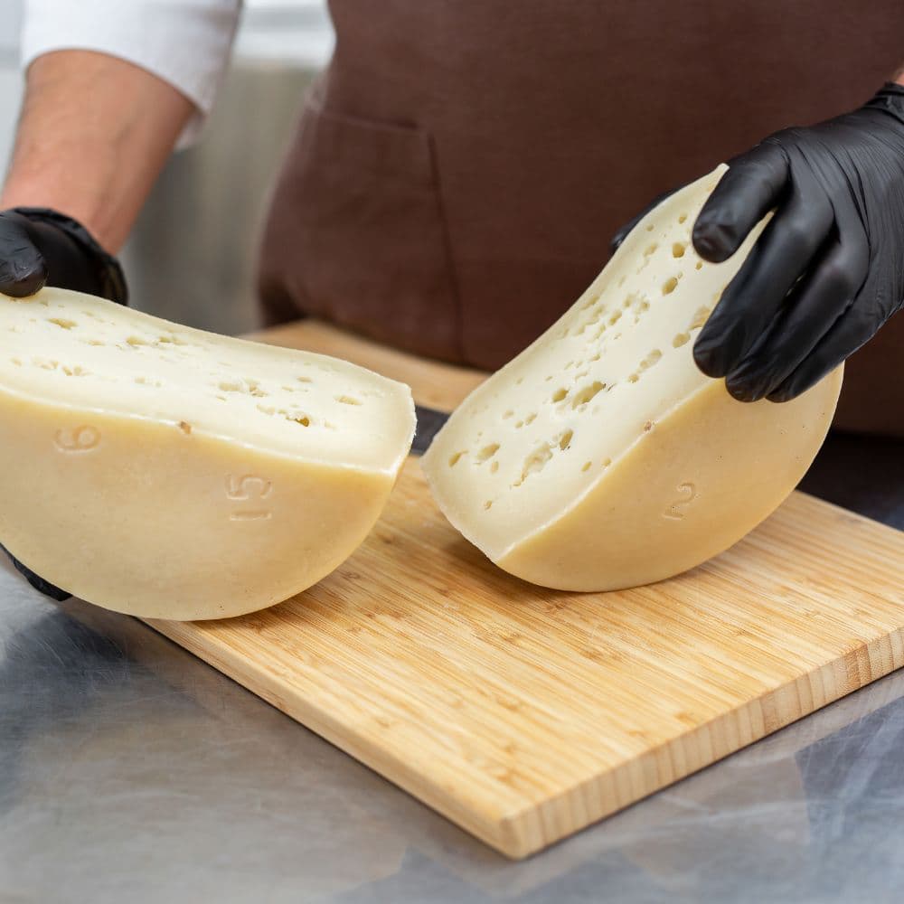 Person holding two wedges of cheese on a wooden cutting board.