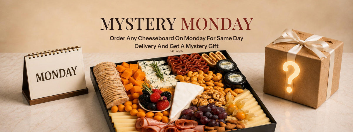Mystery Monday is a promotional campaign visual showing a generously arranged cheese board with assorted cheeses, cured meats, crackers, fruits, nuts, and gourmet accompaniments, paired with a wrapped mystery gift. Discover cheeseboard Dubai, cheese platter Dubai, and charcuterie Dubai from The Cheese Man. Enjoy fresh delivery across the UAE.