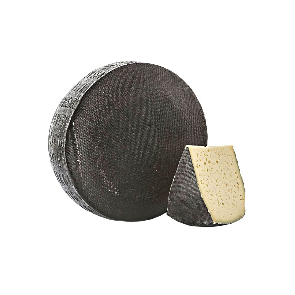 Round black asiago cheese wheel with a wedge cut out on a white background